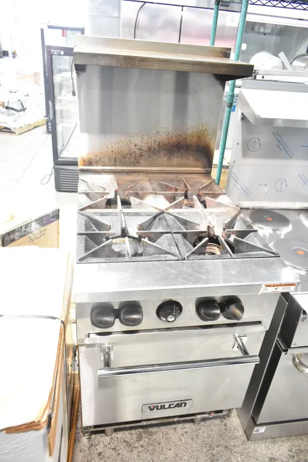 Vulcan commercial gas range with 4 burners, oven, over shelf, and backsplash. Used condition. Brand logo on front panel.