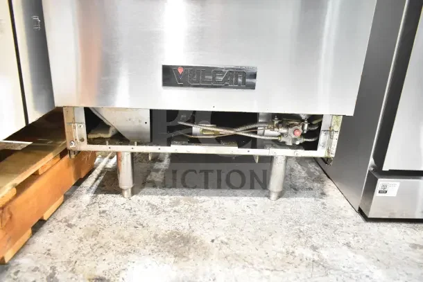 Vulcan Commercial 4 Burner Gas Range with oven, over shelf, and back splash. Visible logo, sturdy metal legs.