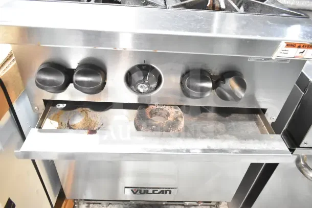 Vulcan commercial 4-burner gas range with oven, featuring knobs, shelf, and backsplash. Used condition with visible wear.