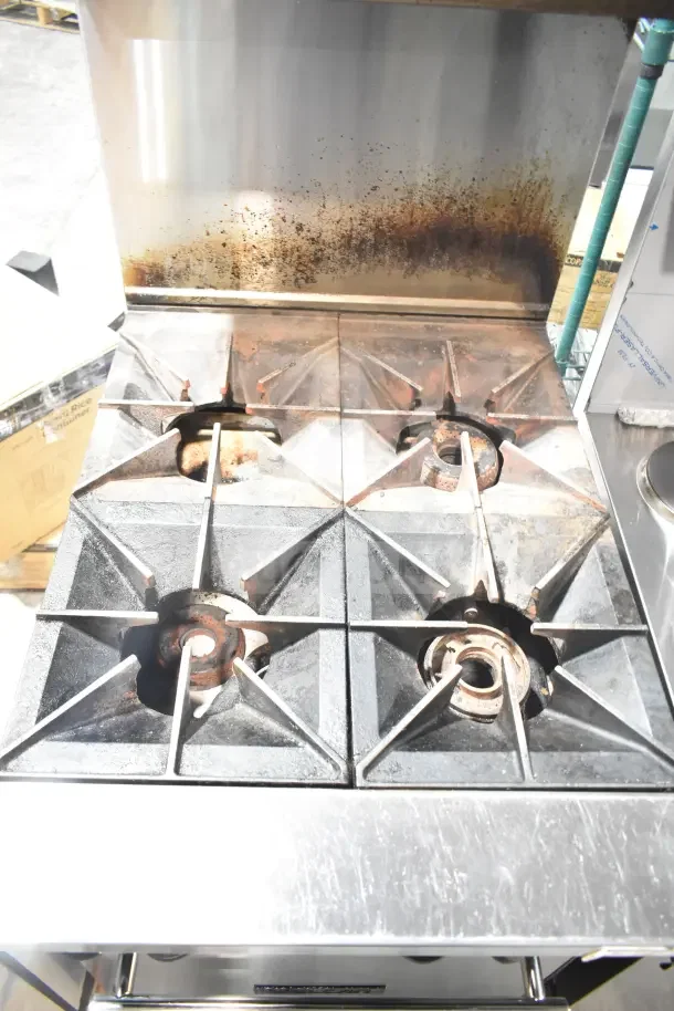 Vulcan commercial gas-powered 4-burner range with oven, over shelf, and backsplash. Shows signs of wear; ideal for professional kitchens.