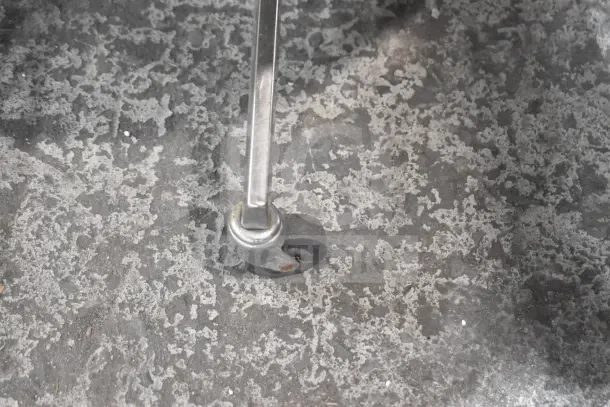 Caster wheel of an armchair, silver frame and black wheel on a textured gray surface, showing slight rust.