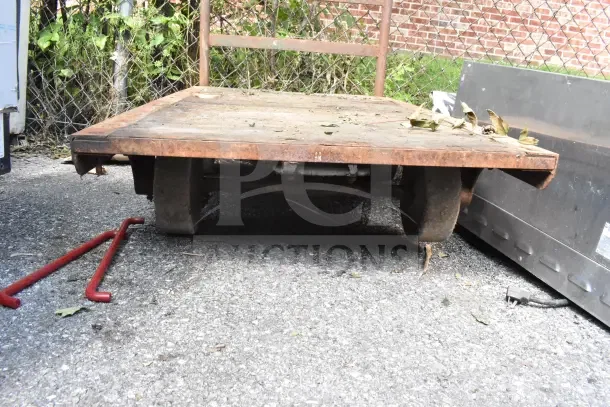 Flat top cart with commercial casters, metal frame, and wooden surface, showing signs of wear and outdoor exposure.