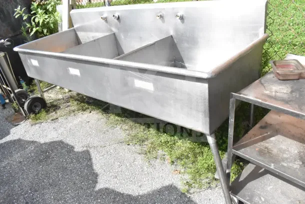 Commercial 3 bay stainless steel sink, used condition, featuring three separate compartments and wall-mounted faucets.