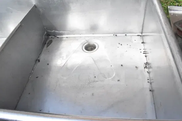 Commercial 3 bay stainless steel sink, showing interior condition with some debris, highlighting durability and spaciousness.