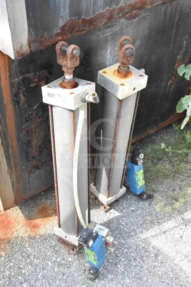Pair of Miller W AL84B2B pneumatic cylinders, showing rust and wear, labeled with "201" marking, outdoor setting.
