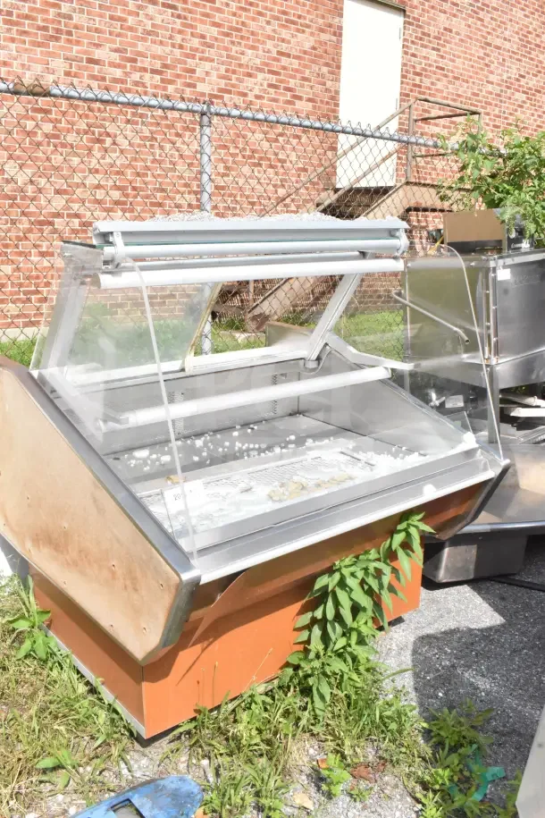 Commercial floor-style display case merchandiser with broken glass, exterior wear, and a stainless steel body.