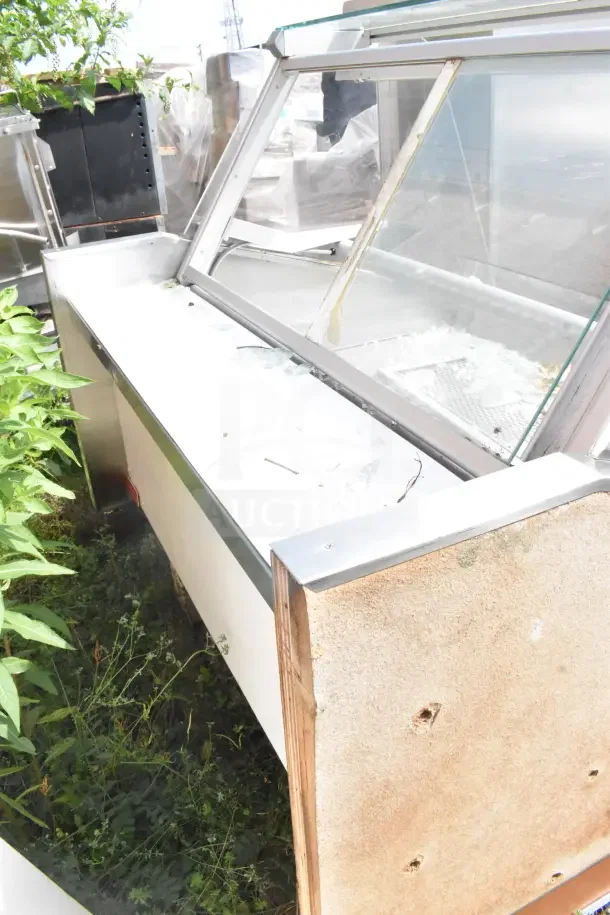 Commercial floor style display case merchandiser with broken glass, stainless steel frame, worn exterior, suited for retail use.