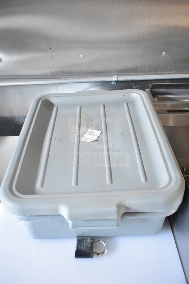 Closed grey storage container with a padlock, placed on a white surface inside a metal food trailer setting.
