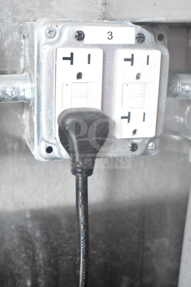 Close-up of electrical outlet with black plug connected, inside 2021 Rock Solid Cargo 8.5'x24' food trailer.