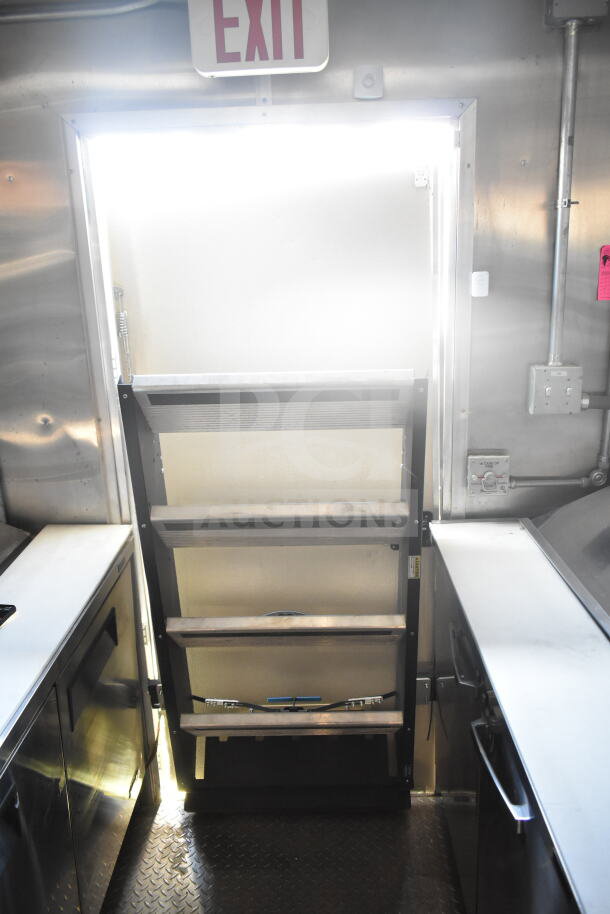 Interior view of 2021 Rock Solid Cargo 8.5'x24' food trailer showing exit door, stainless steel surfaces, and shelving.