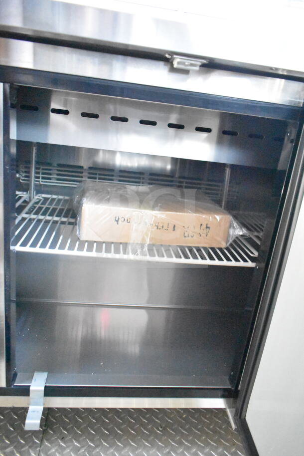 Interior of a 2021 Rock Solid Cargo food trailer showing a stainless steel refrigeration unit with shelving and a boxed item.