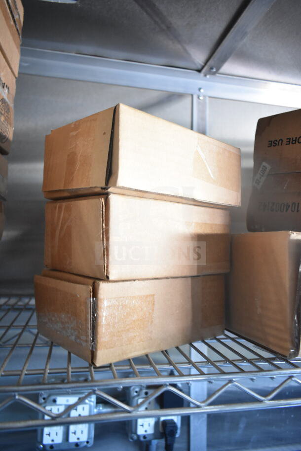 Stacked cardboard boxes on a metal shelf inside the 2021 Rock Solid Cargo food trailer. Electrical outlets visible below.