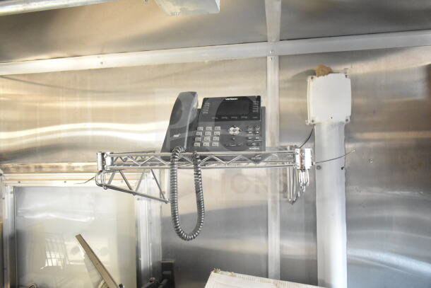Interior view of a 2021 Rock Solid Cargo Food Trailer, showing a mounted phone on a metal shelf, stainless steel walls, and part of the ventilation system.
