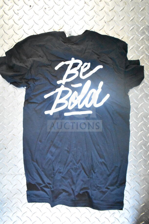 Black t-shirt with "Be Bold" in white text, laid on a diamond plate surface.