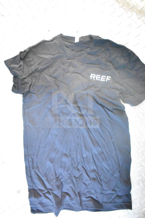 Black T-shirt with "REEF" logo on chest, laid on a textured surface.