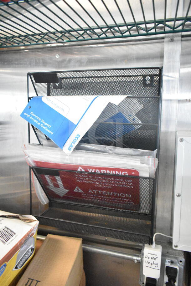 Metal wall organizer with service report folders, warning signs, and a device labeled "Do Not Unplug" in a 2021 Rock Solid Cargo food trailer.