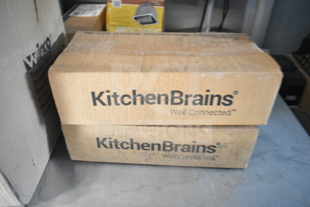 Cardboard boxes labeled "KitchenBrains Well Connected" stacked on a metal surface in a storage area.