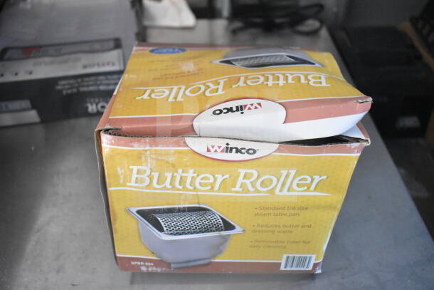 Winco butter roller box on metal surface; features include standard 1/6 size pan and removable roller; packaging shows signs of wear.