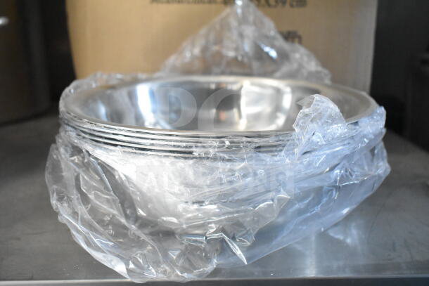 Stack of stainless steel mixing bowls wrapped in plastic, new condition, on a metal surface.