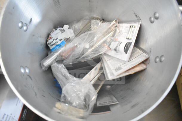 Interior of a large metal pot containing various kitchen tools and packaging, including a clean-up kit and utensils.