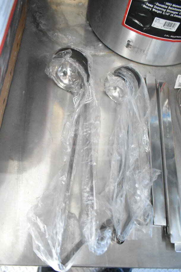 Plastic-wrapped metal utensils on a stainless steel surface, next to a pot with a label.