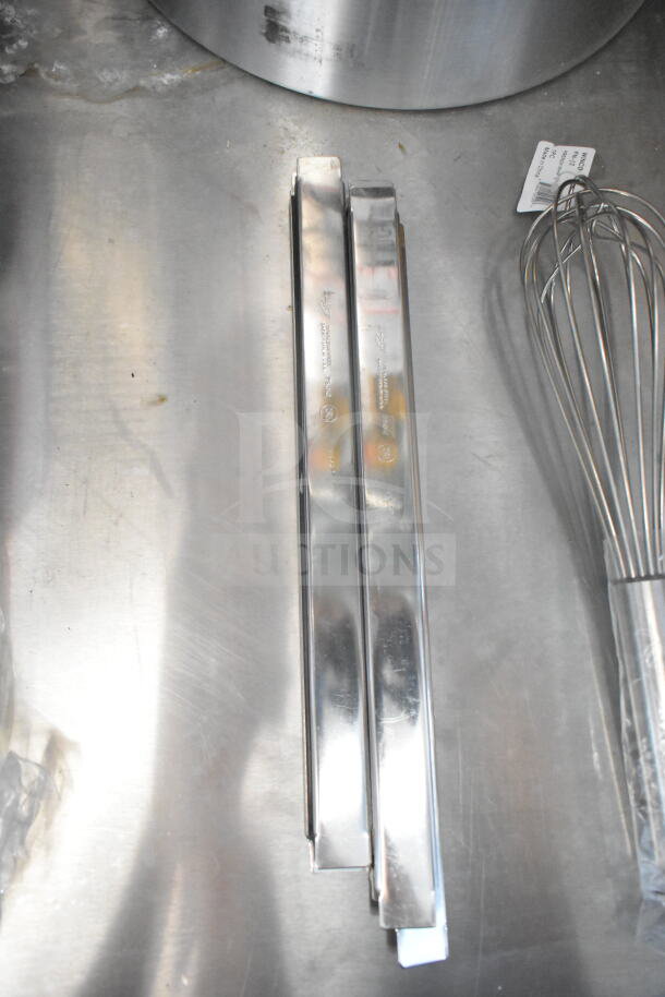 Stainless steel kitchen tongs and a whisk on a metal surface in a food trailer, with a visible inventory tag.