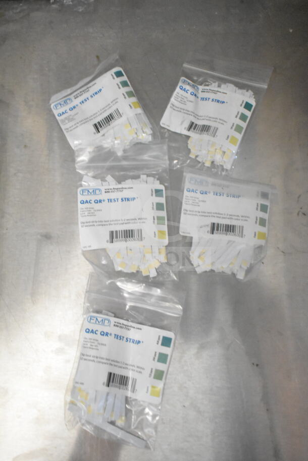 Bags of QAC QR test strips with color scale labels on a metal surface.