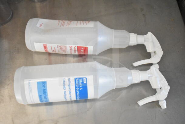 Spray bottles on a metal surface, labeled for sanitizer and glass cleaning.