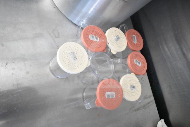 Transparent containers with red and beige perforated lids, on a metal surface. Lids have barcode stickers.