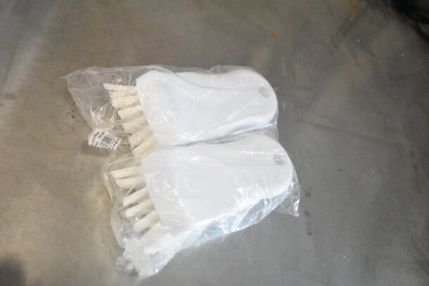 Two sealed plastic bags containing white brushes with long bristles, placed on a metallic surface.