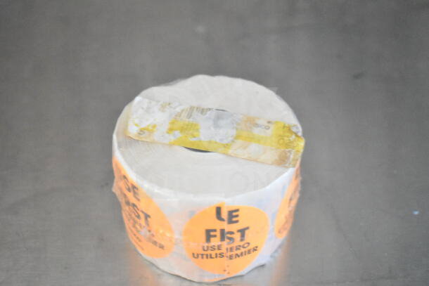 A roll of shrink wrap with orange "Le Fist Use First" stickers, partially obscured yellow label on top.