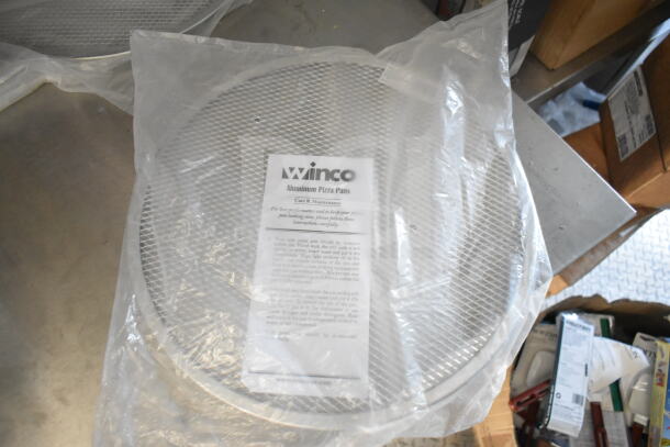 Winco aluminum pizza pans in packaging with care instructions visible, placed on a table.
