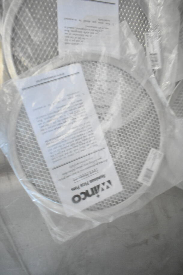 Aluminum pizza pans with mesh, wrapped in clear plastic, labeled “Winco,” against a metallic surface.