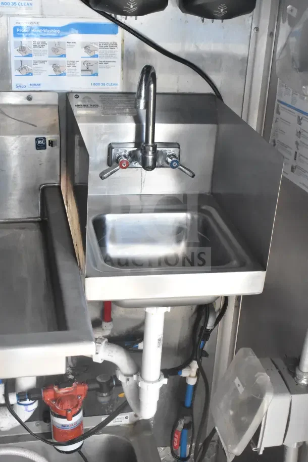 Stainless steel sink with hot and cold water taps in a 2021 Rock Solid Cargo food trailer, includes plumbing components.