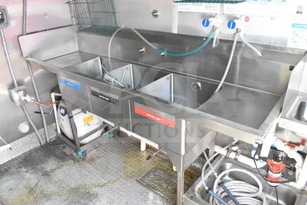 2021 Rock Solid Cargo food trailer interior with a triple sink, labeled water lines, and drainage hoses.