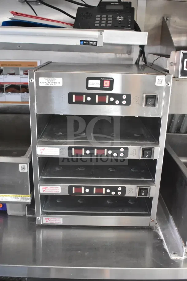 Stainless steel warming drawers in a 2021 Rock Solid Cargo food trailer. Features digital controls and caution labels.