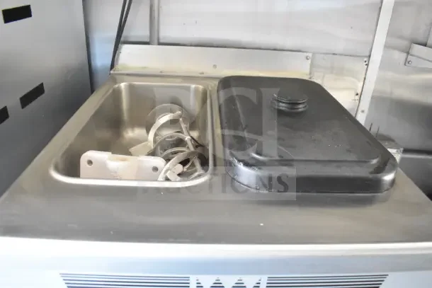 Interior view of 2021 Rock Solid Cargo food trailer sink with a black lid and metal attachments, part of the refrigeration suite.