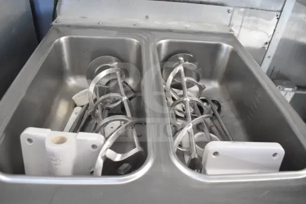 Food trailer interior showing dual sinks with utensils and components from Taylor milkshake machine. Stainless steel finish.