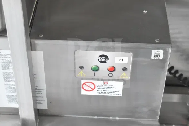 Stainless steel control panel of the AyrKing appliance in a Texino food trailer, featuring red and green buttons, with safety labels.