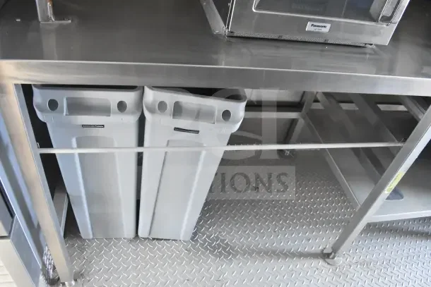 Stainless steel counter with Panasonic NE-1051 microwave, two commercial bins beneath, on diamond plate flooring in 2021 Texino trailer.