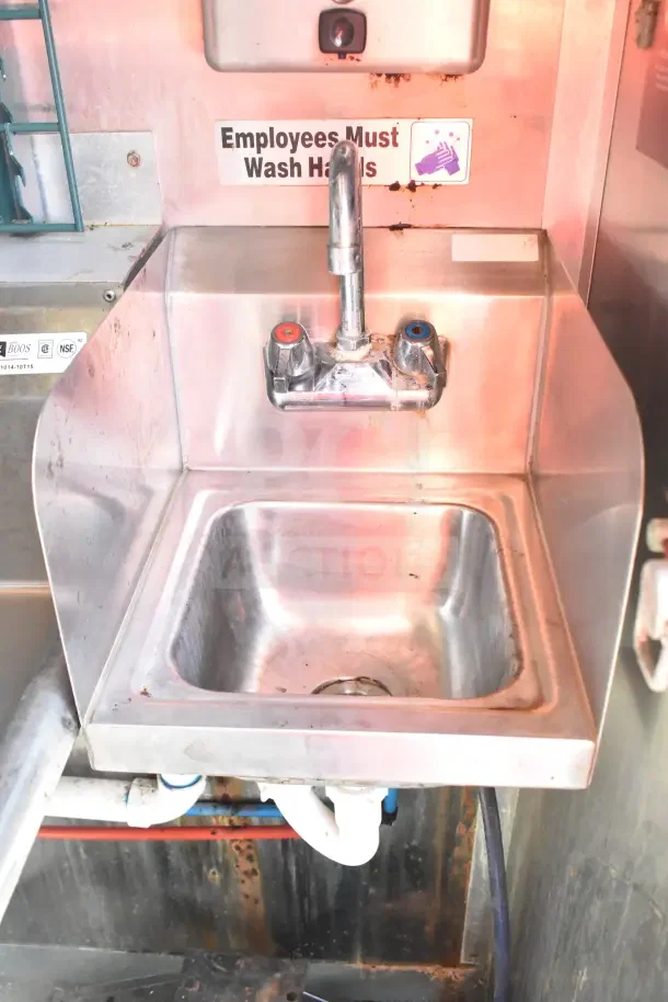 Stainless steel sink with a dual faucet in a 2020 Diamond Cargo kitchen trailer. Sign reads "Employees Must Wash Hands."