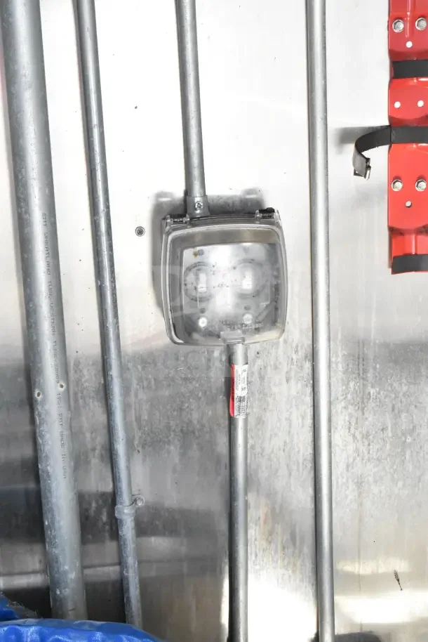 Outdoor electrical box on the interior wall of a commercial kitchen trailer, showing galvanized pipes and wiring.