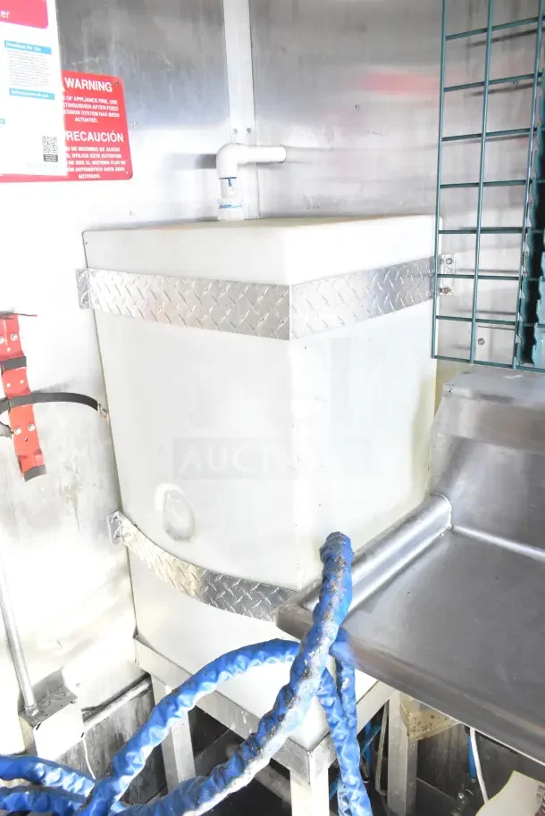 Diamond Cargo trailer interior with mounted white storage tank, blue hoses, and metal fixtures. Safety warning sign visible.