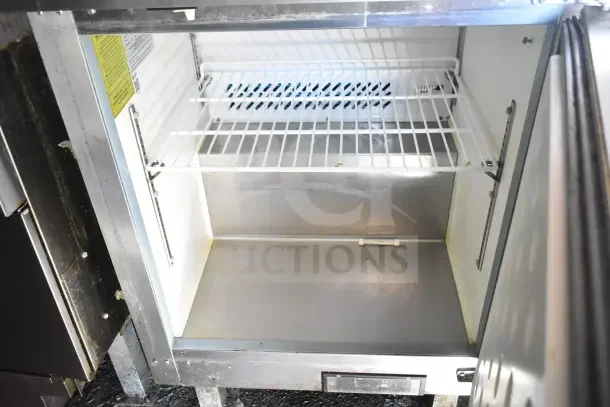 Interior of refrigeration unit in 2020 Diamond Cargo kitchen trailer, featuring a wire shelf and open stainless steel floor.