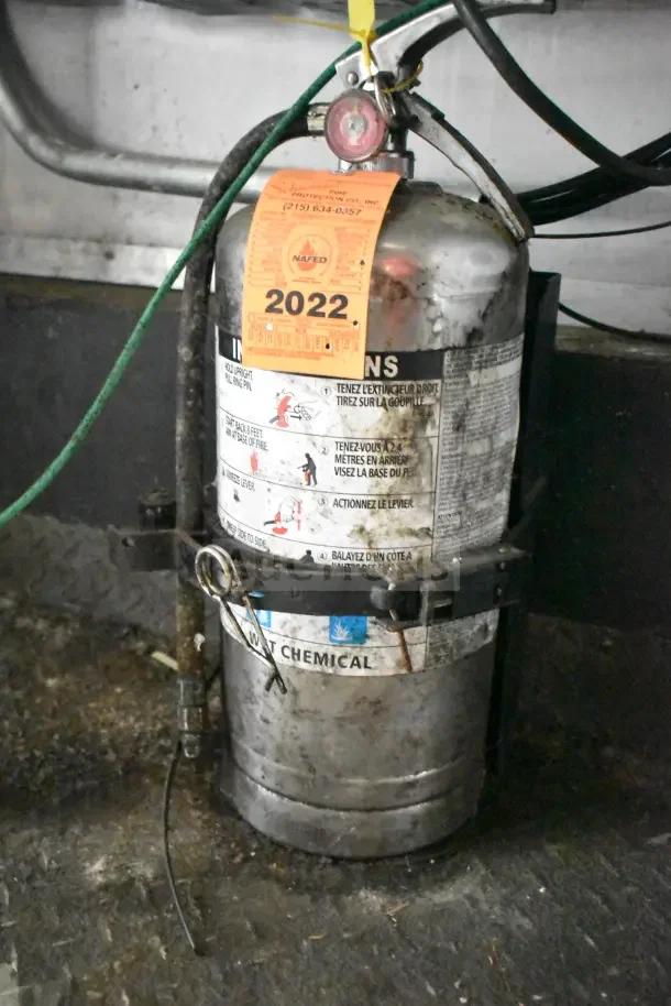 Fire extinguisher in a Diamond Cargo kitchen trailer with inspection tag labeled 2022, attached and secure with hoses.