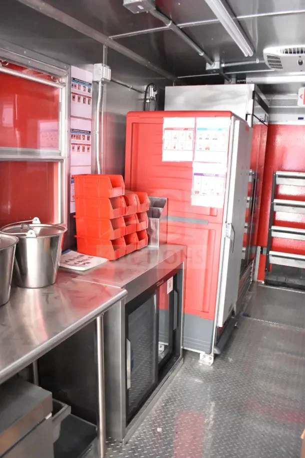 2022 Rock Solid Cargo 8.5x28 Ghost Kitchen Trailer interior, shown with stainless counters, Turbo Air refrigeration, and red storage bins.