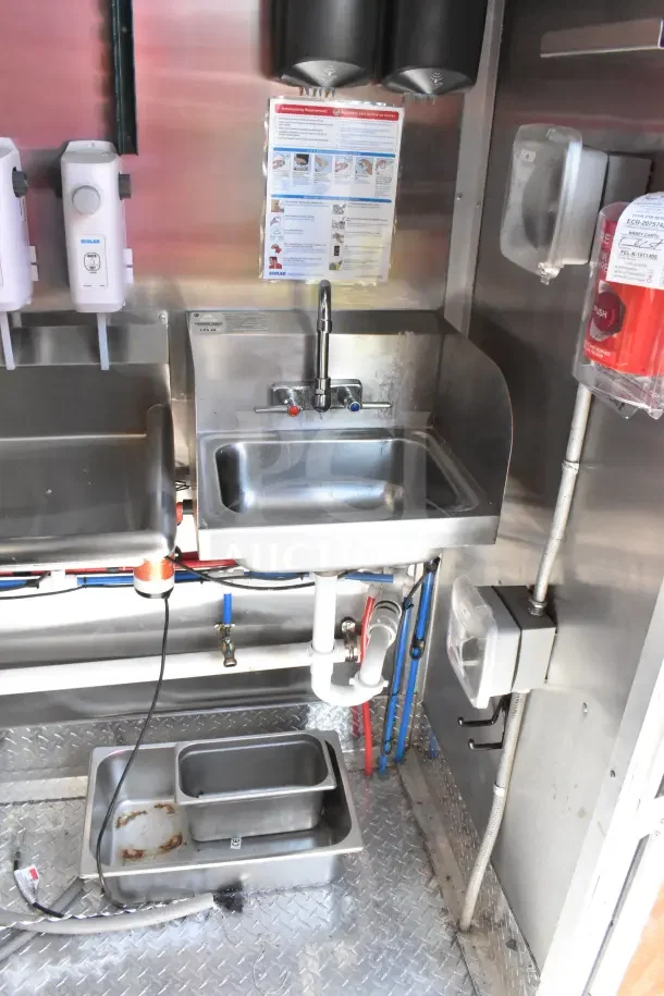Interior of 2022 Rock Solid Cargo Ghost Kitchen Trailer, featuring stainless steel sink with faucet, soap dispensers, and plumbing.