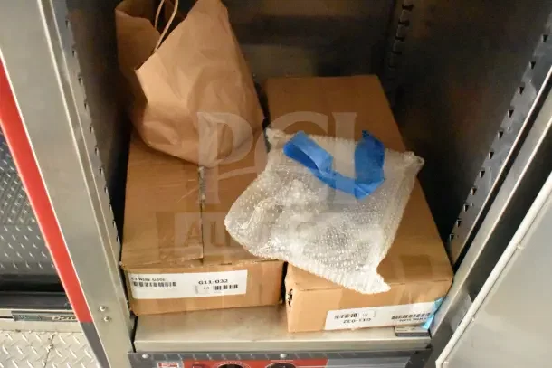 Boxes and brown paper bag stored in trailer cabinet. Labels show model G11-032. Blue-taped bubble wrap visible.