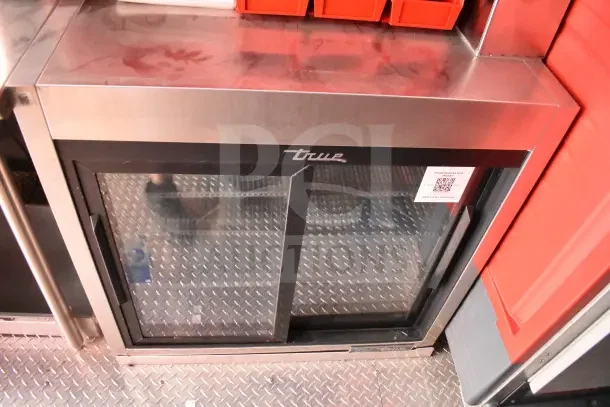 True commercial undercounter glass-door refrigerator inside a 2022 Rock Solid Cargo kitchen trailer. Stainless steel top and visible QR code.