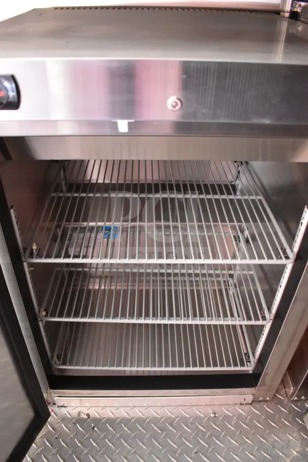 Interior view of the 2022 Rock Solid Cargo 8.5x28 Ghost Kitchen Trailer fridge with wire racks and stainless steel finish.